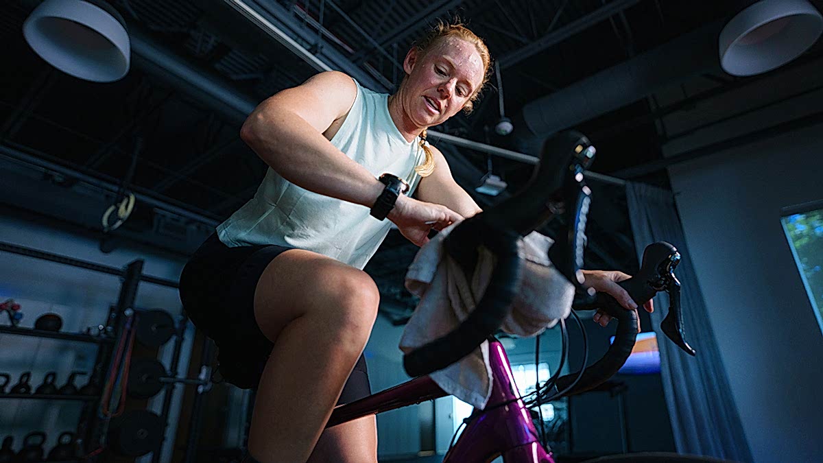 Effective 60 Minute Cycling Workouts Female Cyclist On Indoor Trainer Bike Looking At Watch During A Workout
